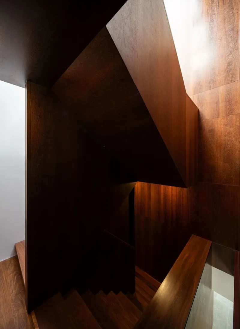 Looking down the dark wood stairwell with warm light grazing the paneled surfaces