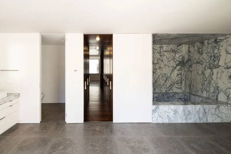 Open room with white sliding doors and gray-veined marble bathtub surround