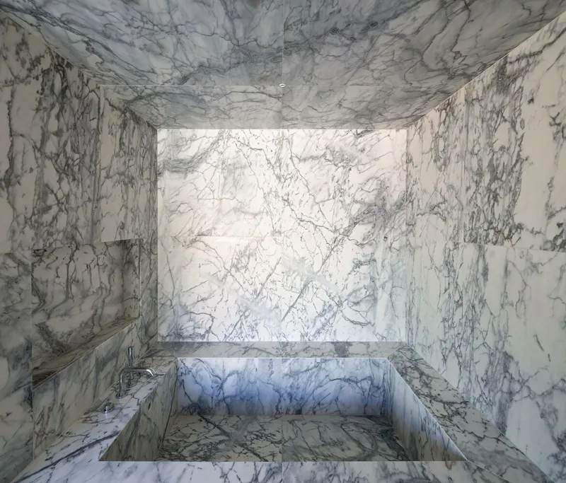 Sunken marble bath surrounded by book-matched veined stone walls and ceiling in bright daylight