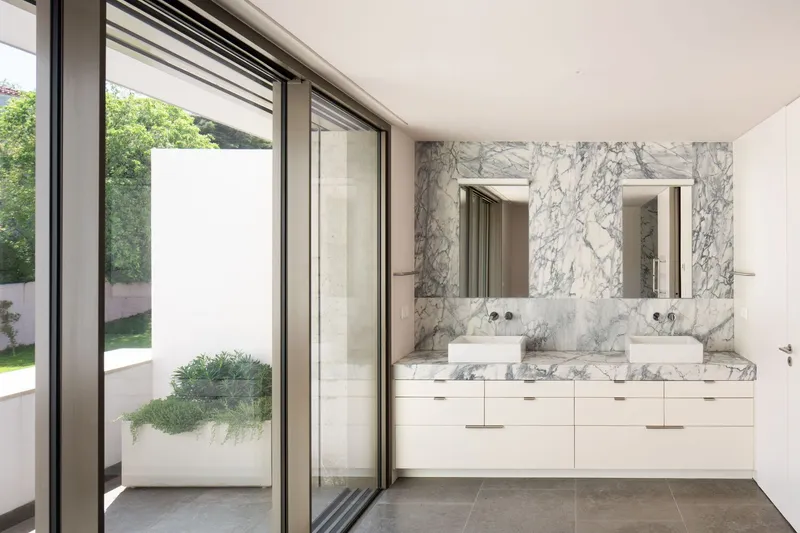 Bathroom with dual sinks set in marble vanity opening to courtyard garden beyond