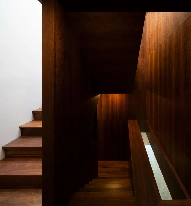 Dark timber staircase ascending through vertical wood-paneled walls with warm indirect lighting below