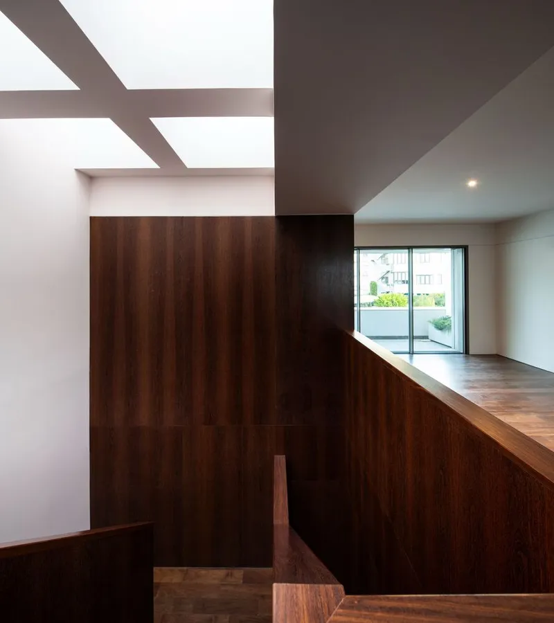 Upper level landing with walnut volume beneath grid skylights overlooking glazed doors to terrace