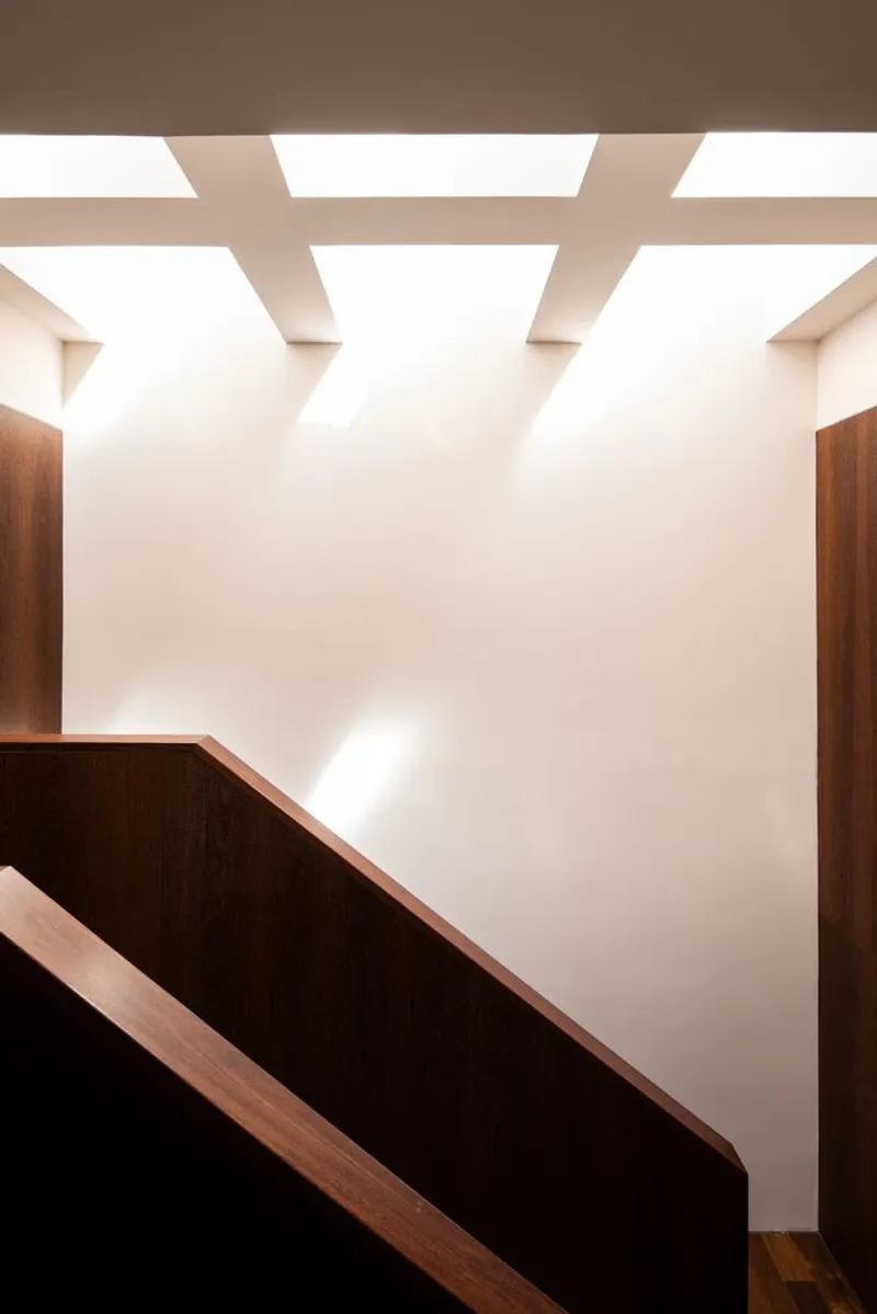 Timber handrail and stair landing beneath cross-pattern skylights casting diffuse daylight on white walls