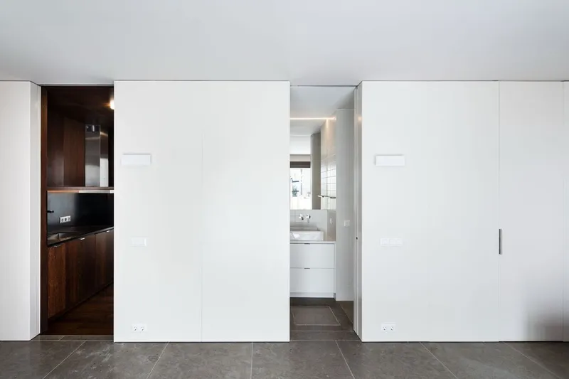 White sliding wall panels concealing a kitchen and bathroom on grey tile flooring