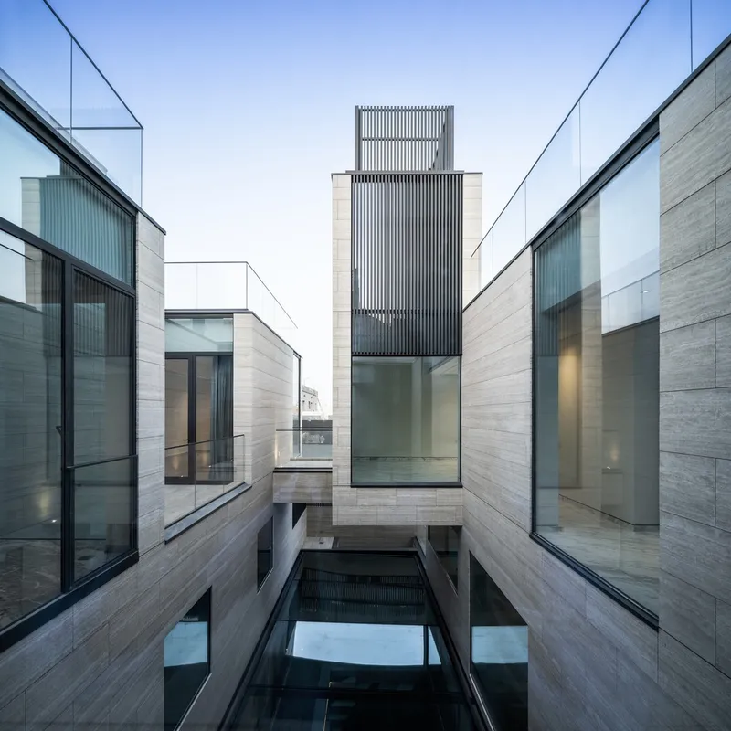 Sunken courtyard framed by horizontal stone cladding and glass walls with a vertical slatted tower above