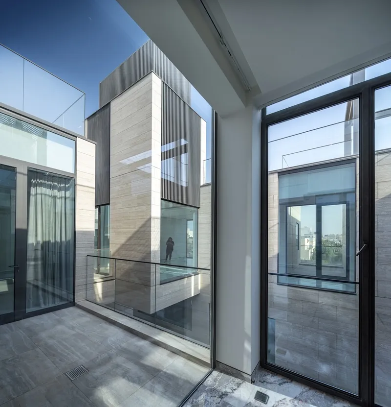 Interior view through floor-to-ceiling glass doors overlooking a multi-level courtyard with a figure visible across the void
