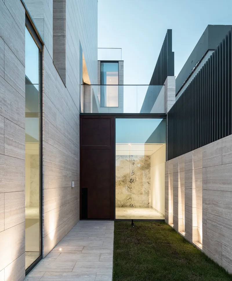 Narrow entry passage with timber door flanked by illuminated stone walls and a glass bridge overhead