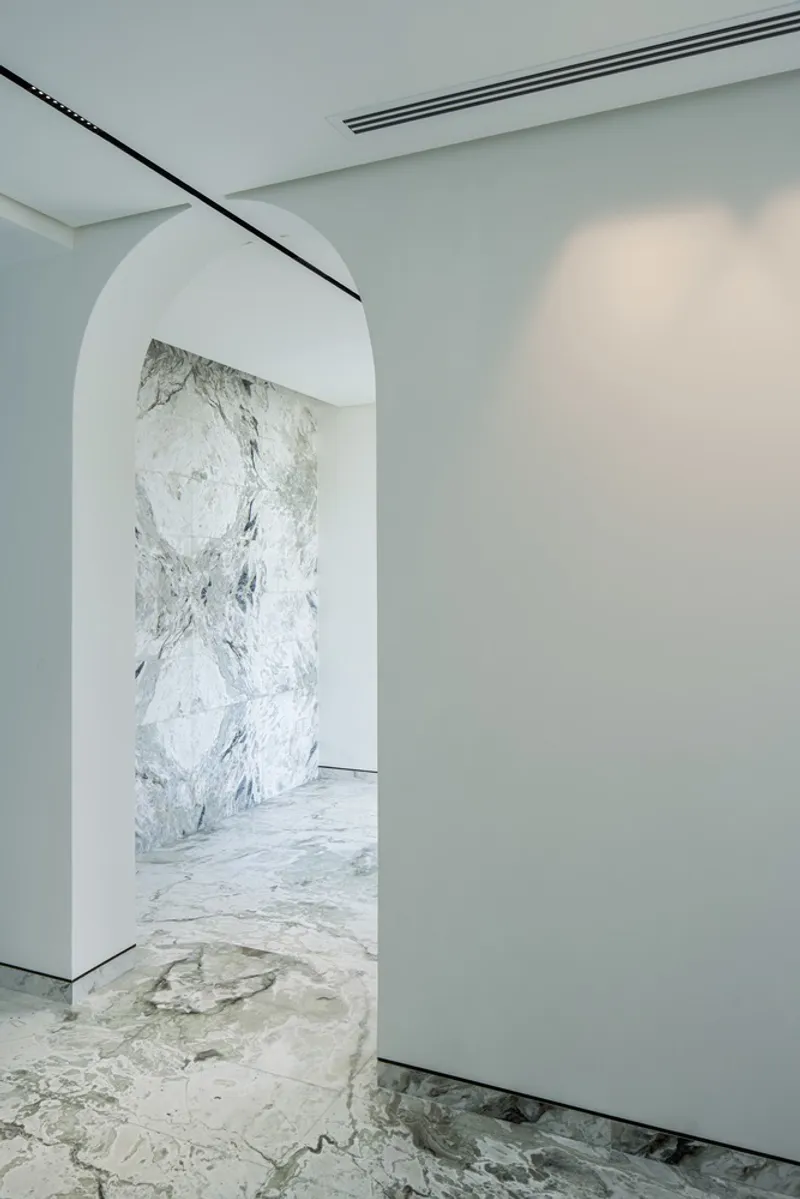Arched doorway framing a white marble feature wall with pale stone flooring in an interior corridor