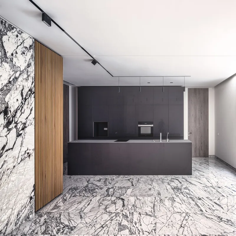 Open kitchen with dark grey island and vertical timber slats beside a white marble wall and floor
