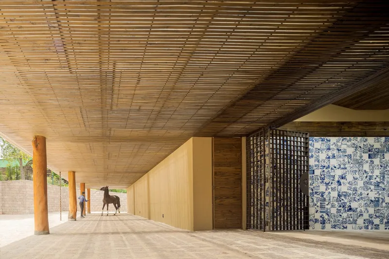 Covered colonnade with timber slat ceiling and blue tile mosaic wall beside a horse