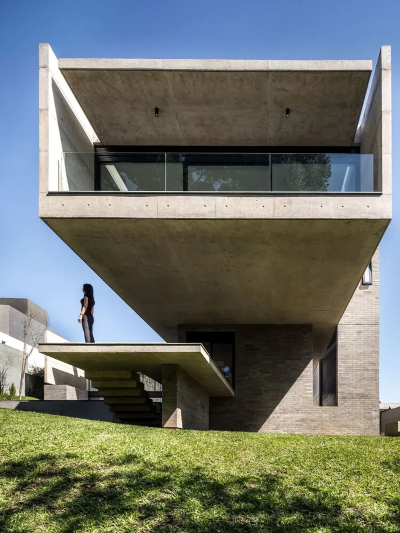Cantilevered concrete volume with glazed balcony and figure standing on the lower terrace
