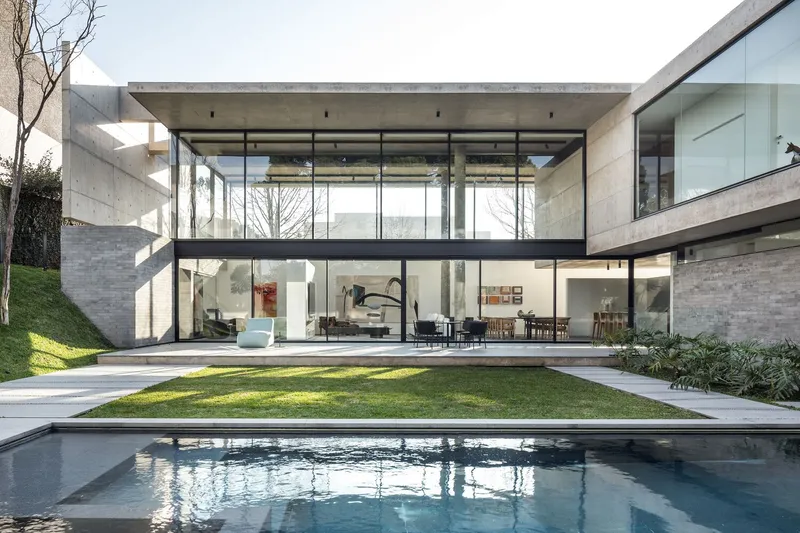 Garden view of the concrete and glass facade with pool and lawn in afternoon light