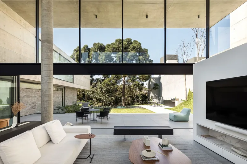 Living room opening to lawn through full-height glazing with exposed concrete soffit and black steel frame