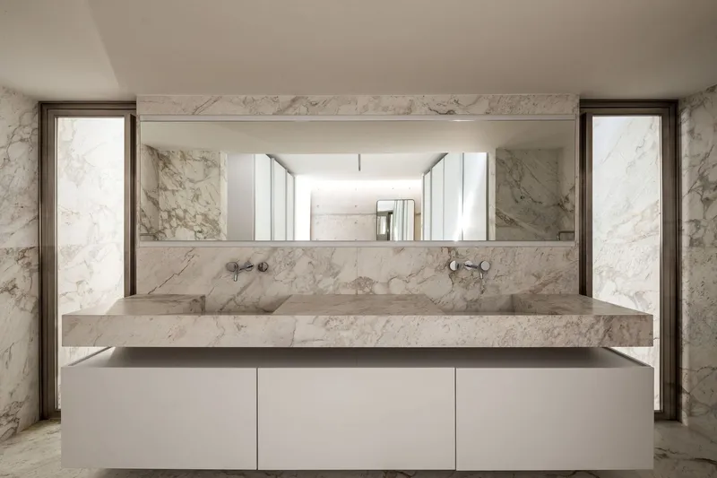 Bathroom vanity with veined marble countertop and backsplash flanked by vertical mirror panels with bronze frames