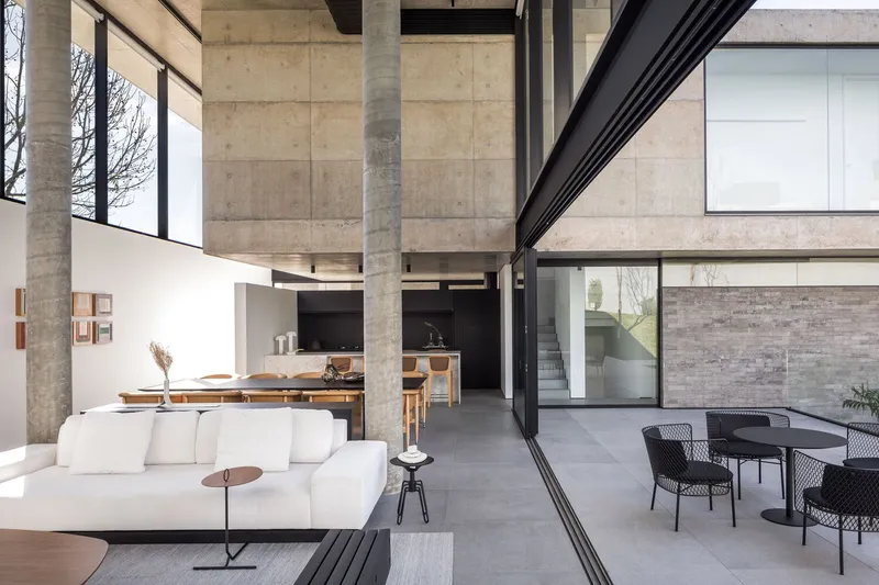 Open-plan living space with concrete columns and exposed ceiling beams connecting interior to outdoor terrace