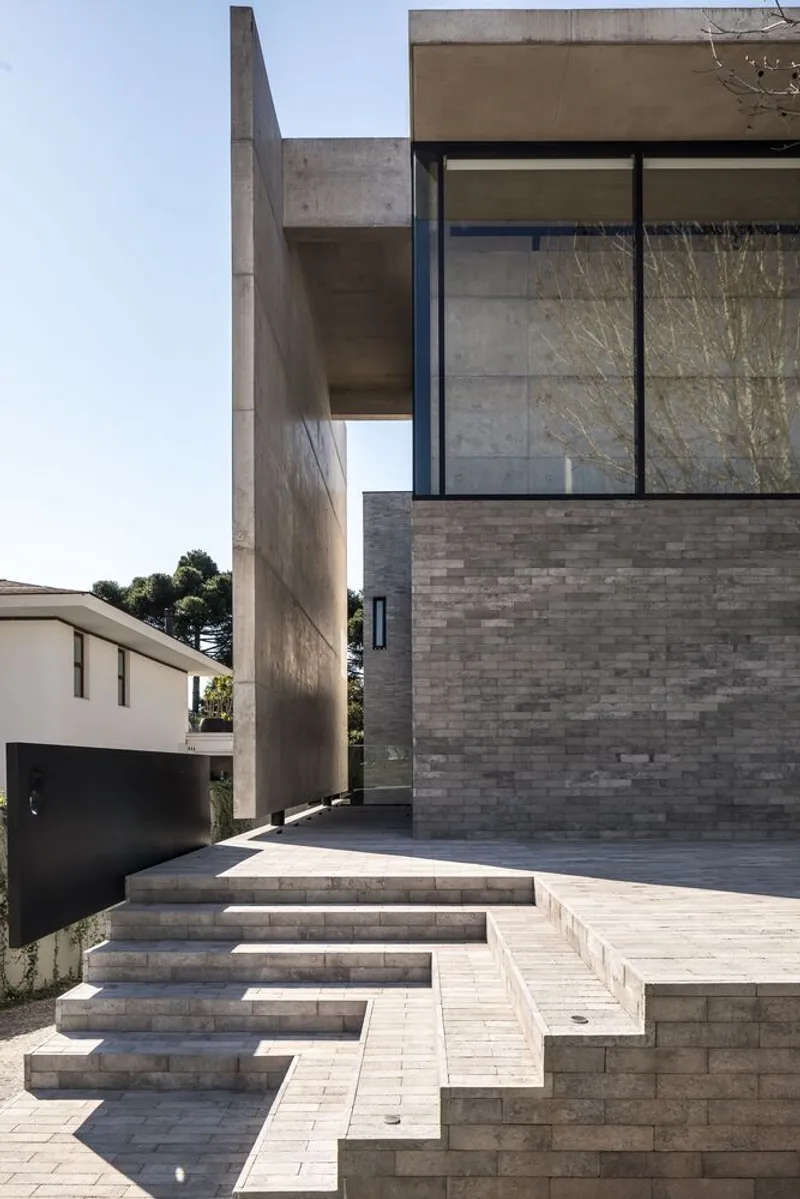 Exterior entry with cantilevered concrete volume above stepped paver terrace and grey brick plinth