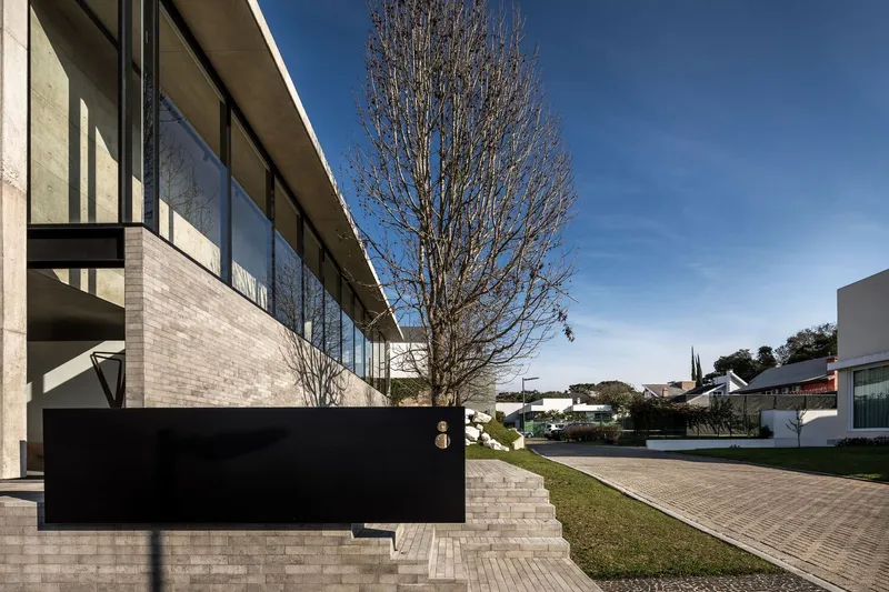 Glazed upper volume on brick base with bare deciduous tree and paved terraced landscape