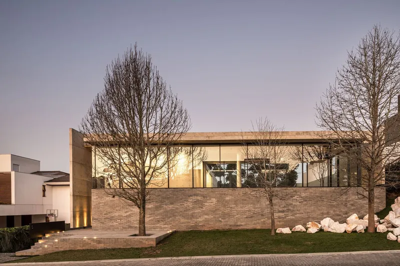 Street facade with brick base and glass upper level framed by two bare winter trees at dusk