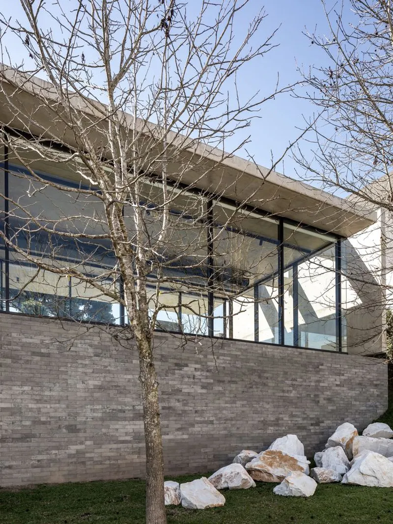 Corner detail of textured brick wall with white stone outcrop and bare tree against glass facade
