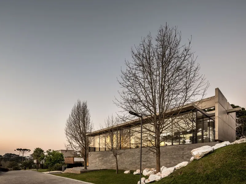 Street view of glass-walled upper floor and bare trees at dusk with illuminated interior
