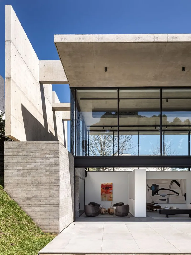 Courtyard view with exposed concrete walls and slabs framing double-height glazed living space below clear blue sky