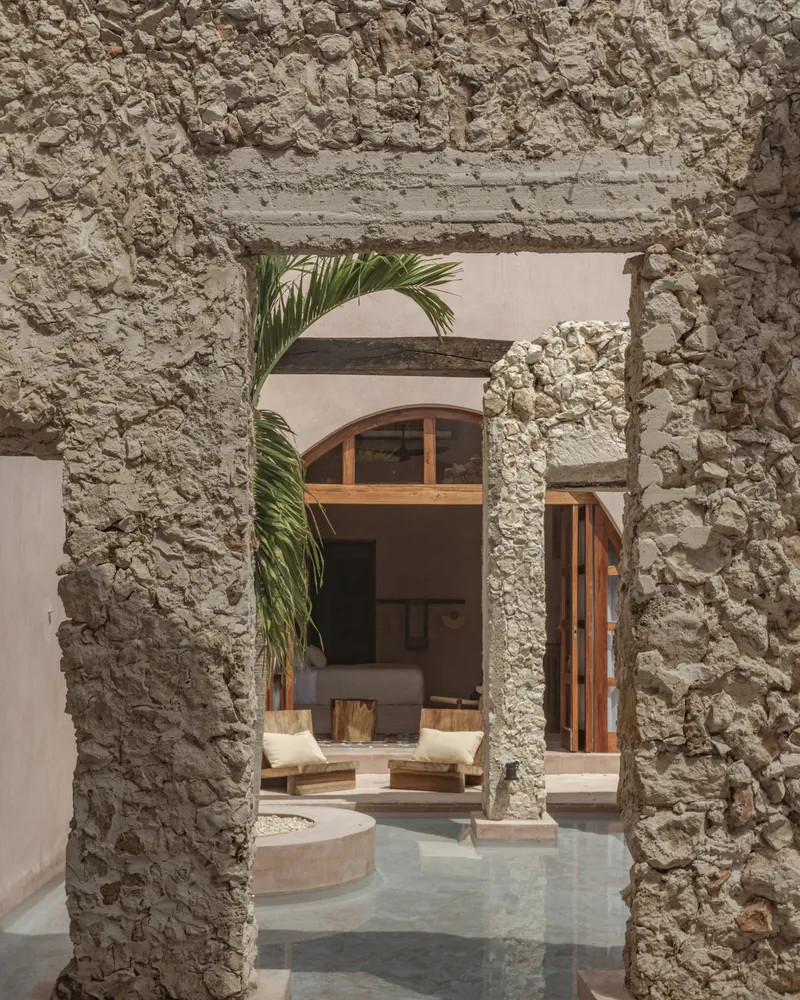View through a ruined stone archway to an interior courtyard with palms and arched timber windows