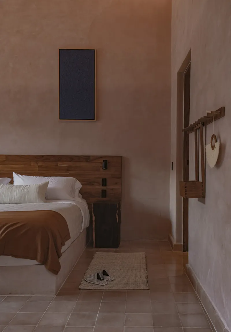 Bedroom with timber-framed bed and earthen plaster walls in warm afternoon light