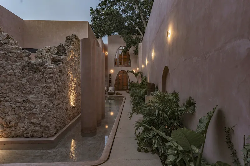 Courtyard passage with preserved stone ruins, rendered walls, arched openings and tropical plantings at dusk