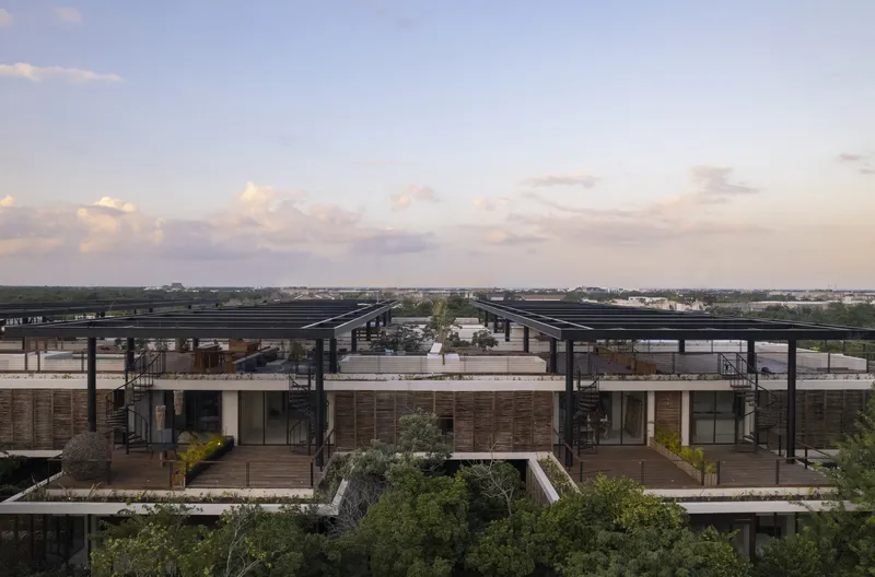Upper residential terraces with timber screens and planted balconies under dark steel roof beams at dusk