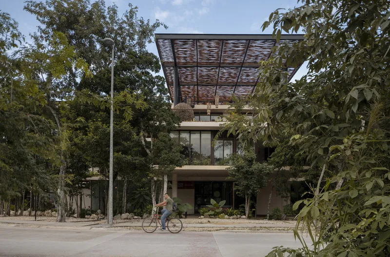 Street view of the tiered facade with horizontal timber louver canopy and cyclist passing on road