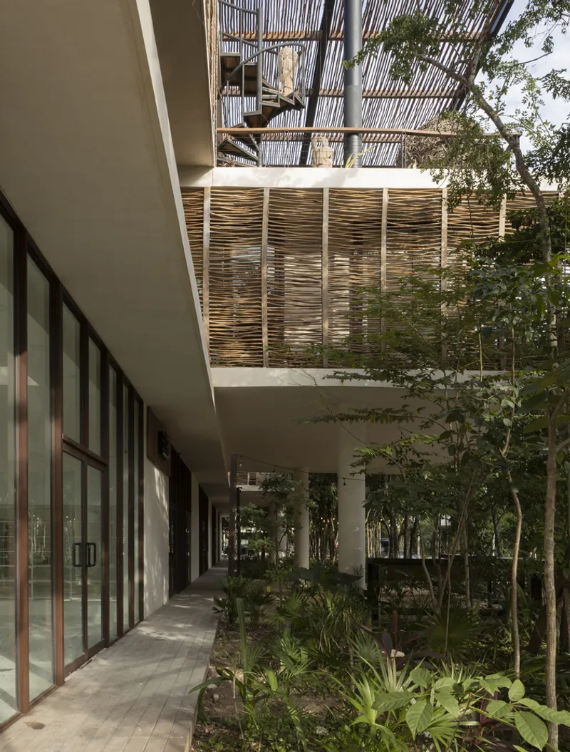 Covered walkway with planted beds and glazed storefronts beneath cantilevered concrete slab and timber screens