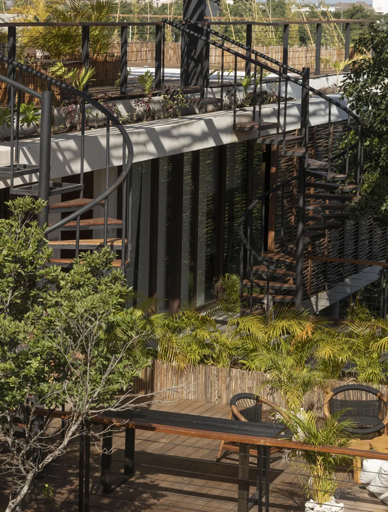 Curved steel staircase descending through planted levels with timber louvers and outdoor seating terrace