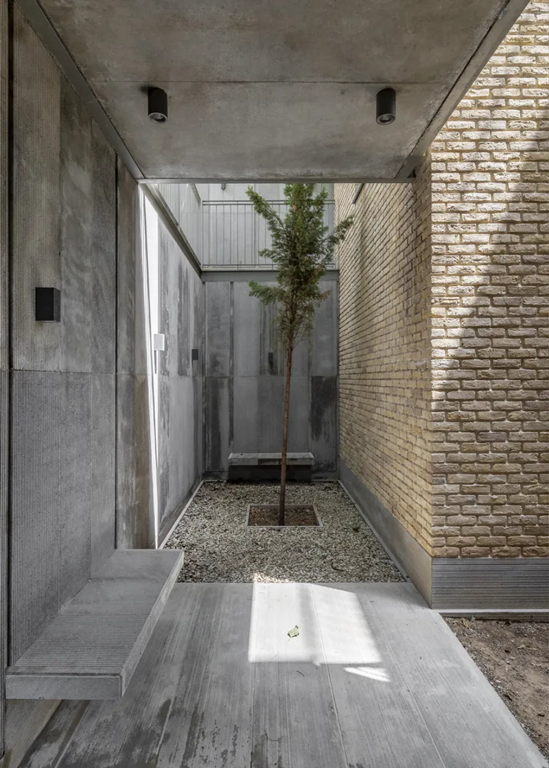 Ground-level courtyard showing concrete walls, buff brick, gravel bed with young tree, and timber decking
