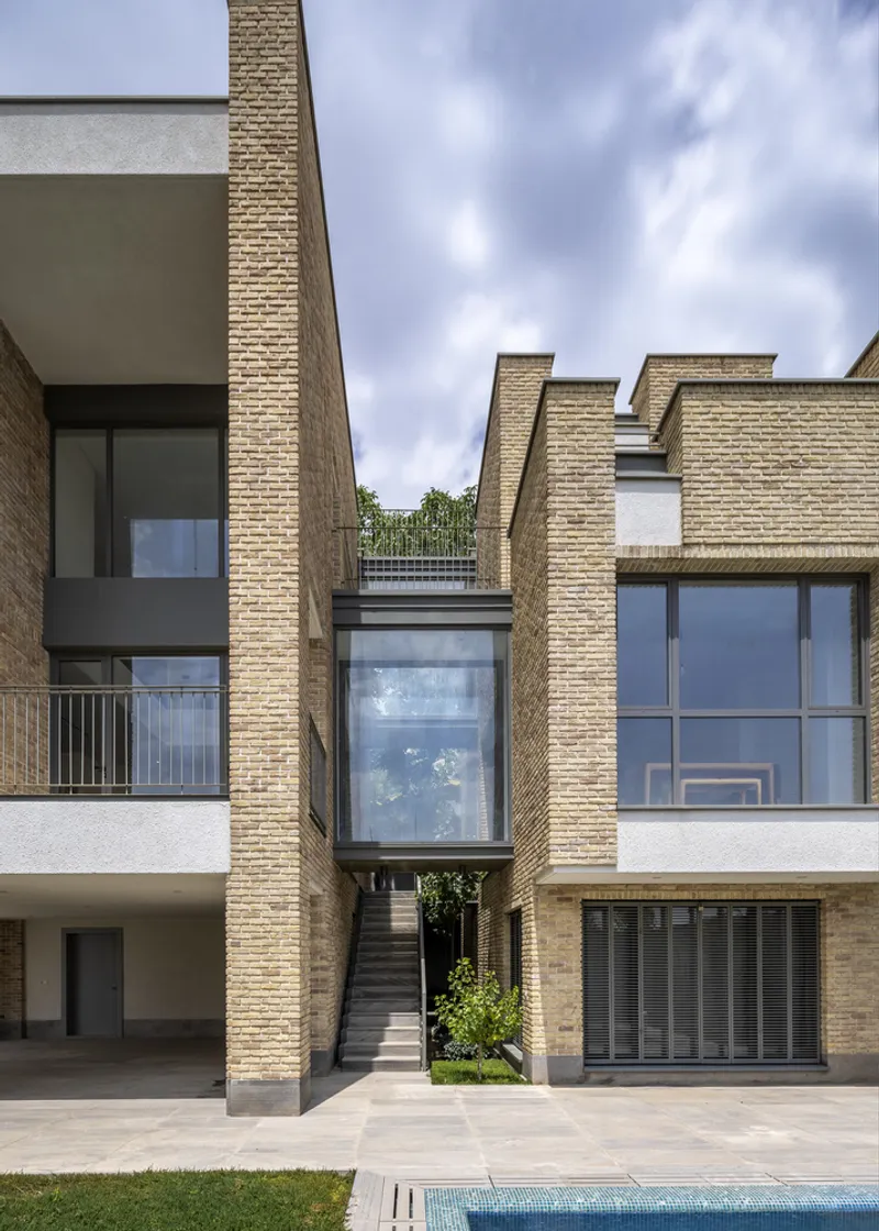 Brick volumes flanking glazed circulation core with external staircase under a cloudy sky