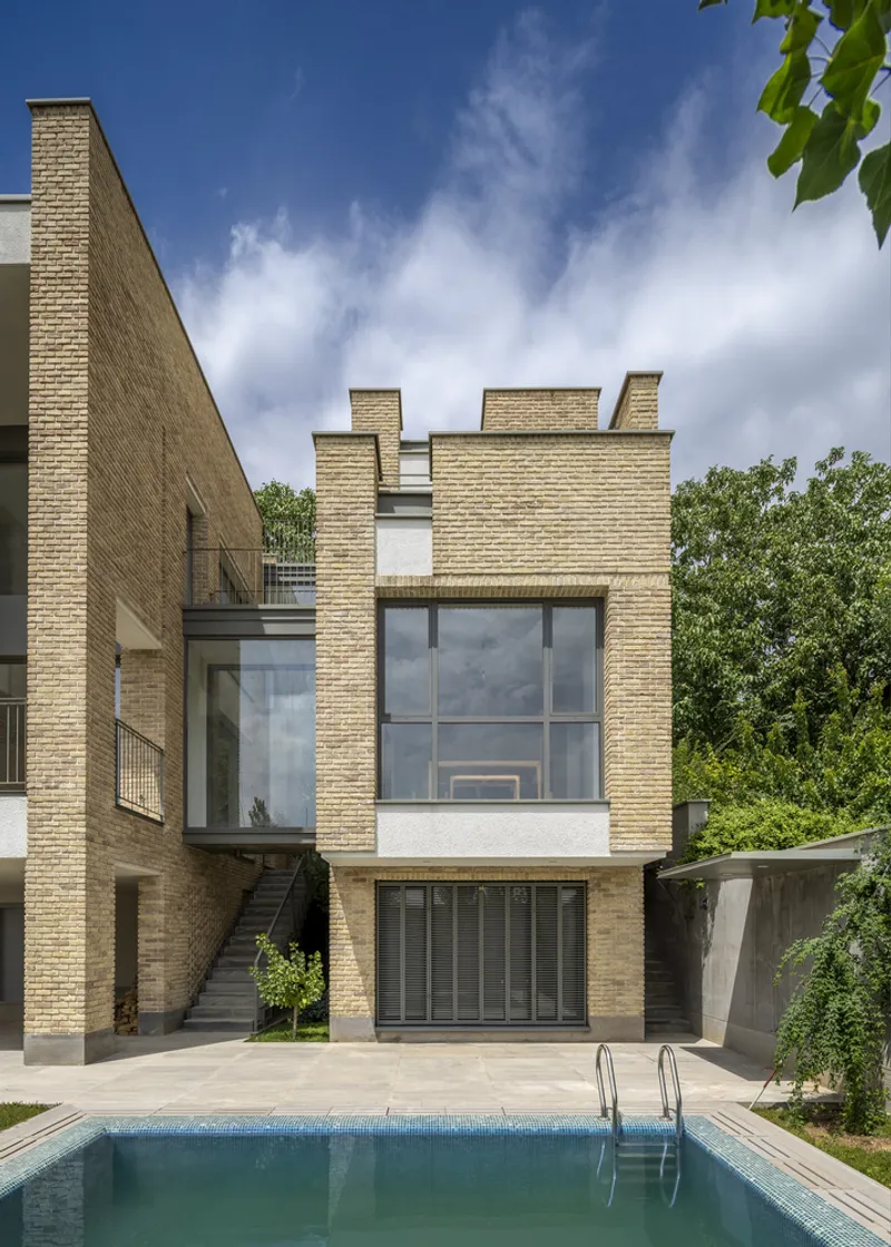 Rear elevation of the buff brick townhouse with large windows overlooking a rectangular swimming pool