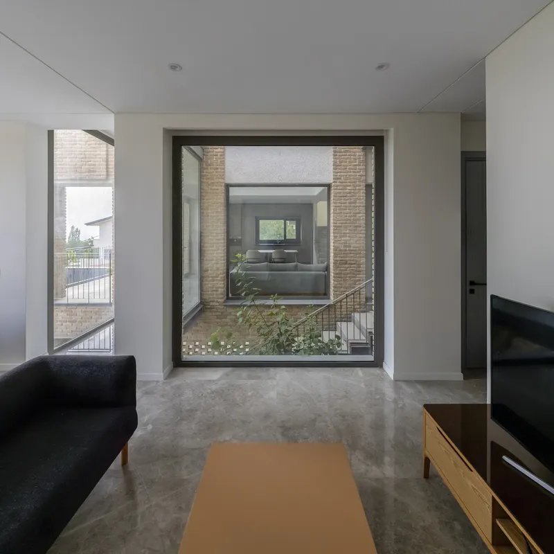 Living room view through a floor-to-ceiling window into the internal courtyard with planted greenery