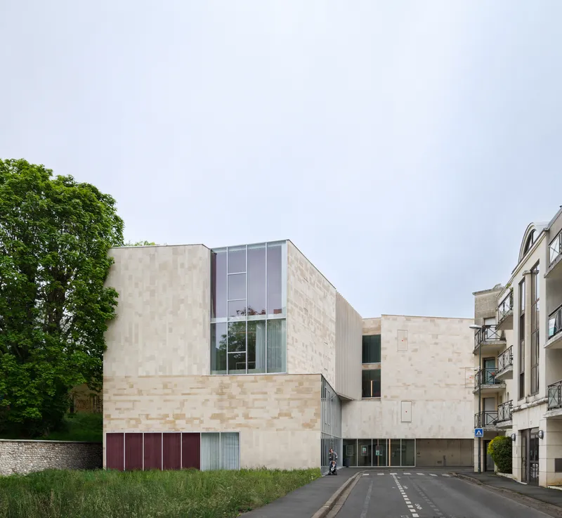Street view of the variegated brick facade with glass stair tower and neighboring buildings under overcast skies