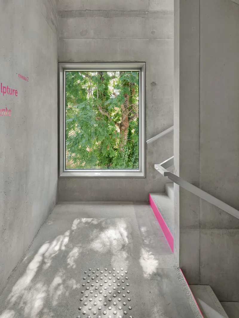 Concrete stairwell with framed window view of green foliage and dappled sunlight on the floor