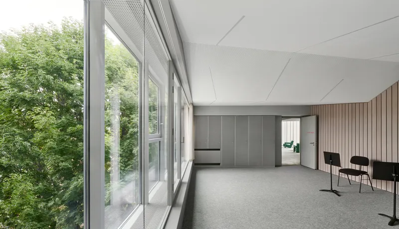 Classroom space with perforated metal ceiling and glazed wall overlooking trees in summer