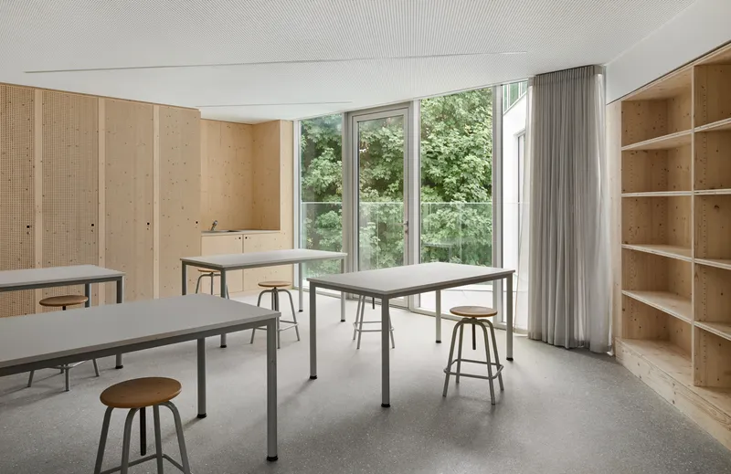 Workshop room with pegboard plywood walls, work tables, stools and shelving near garden windows