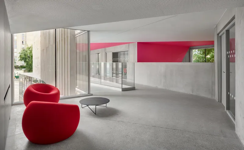 Open corridor with pink wall band and red seating facing glass-enclosed room and exterior views
