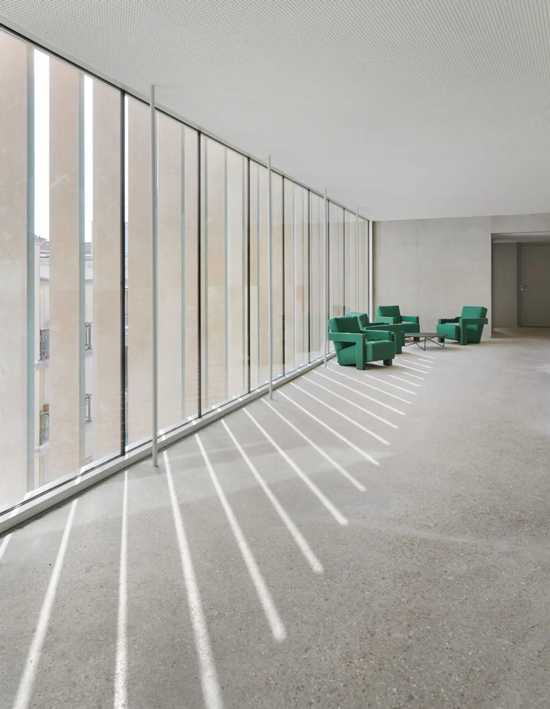 Interior hallway with vertical louver facade casting striped shadows across the terrazzo floor
