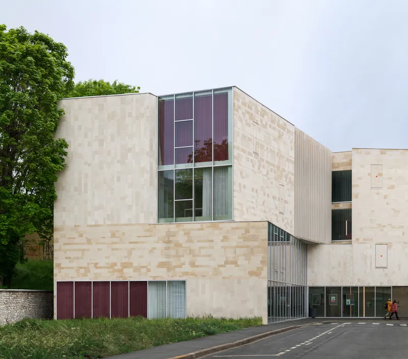 Street view of the chequered stone facade with vertical metal fins and a person in red walking