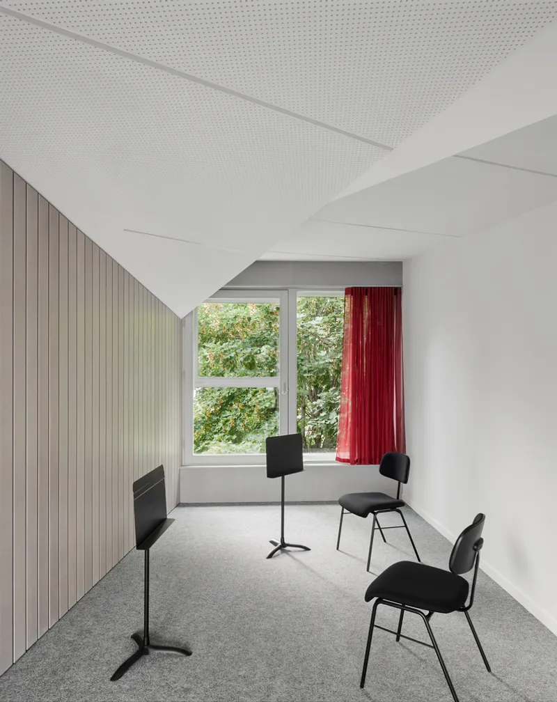 White rehearsal room with perforated acoustic ceiling panels, vertical timber wall cladding and red curtains