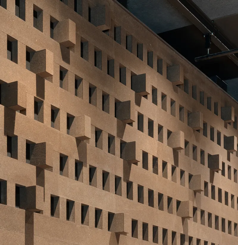 Close-up of the three-dimensional cork acoustic wall with staggered rectangular openings and exposed stage rigging