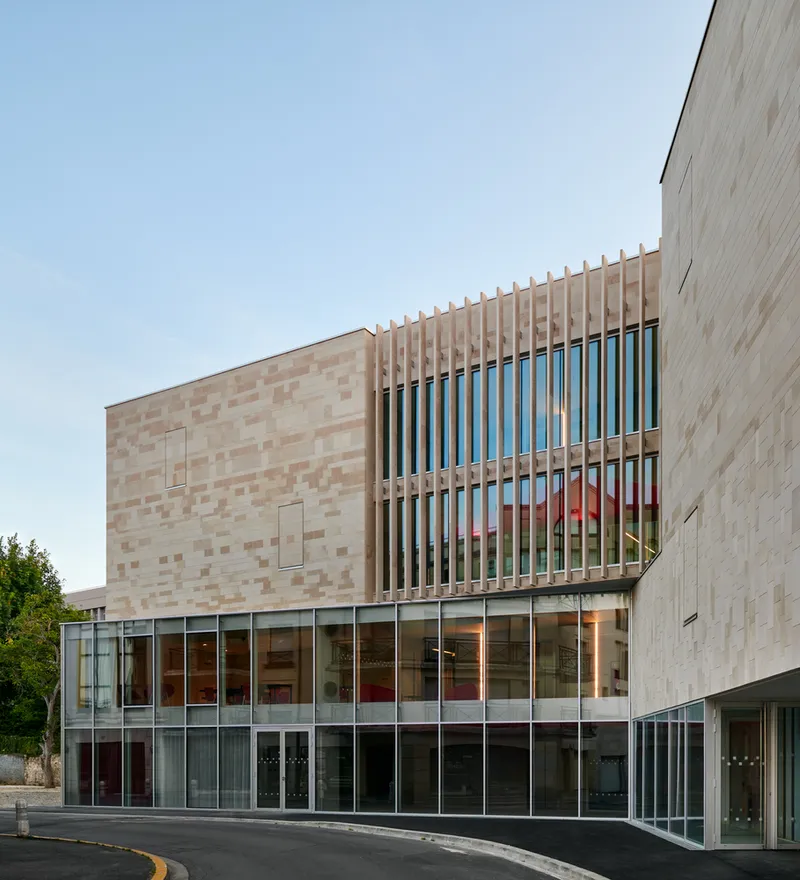 Street view of the timber-louvered upper volume above a glazed ground floor at dusk