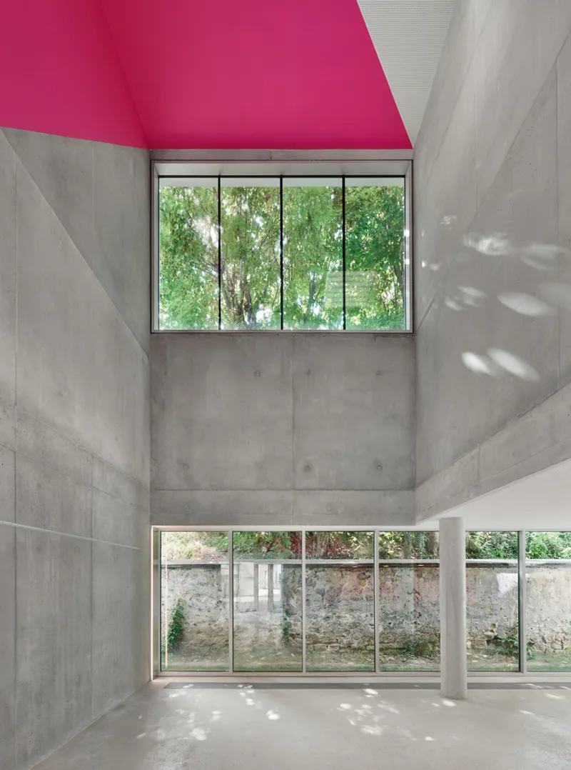 Double-height space with concrete walls, magenta ceiling and horizontal window framing an overgrown garden wall