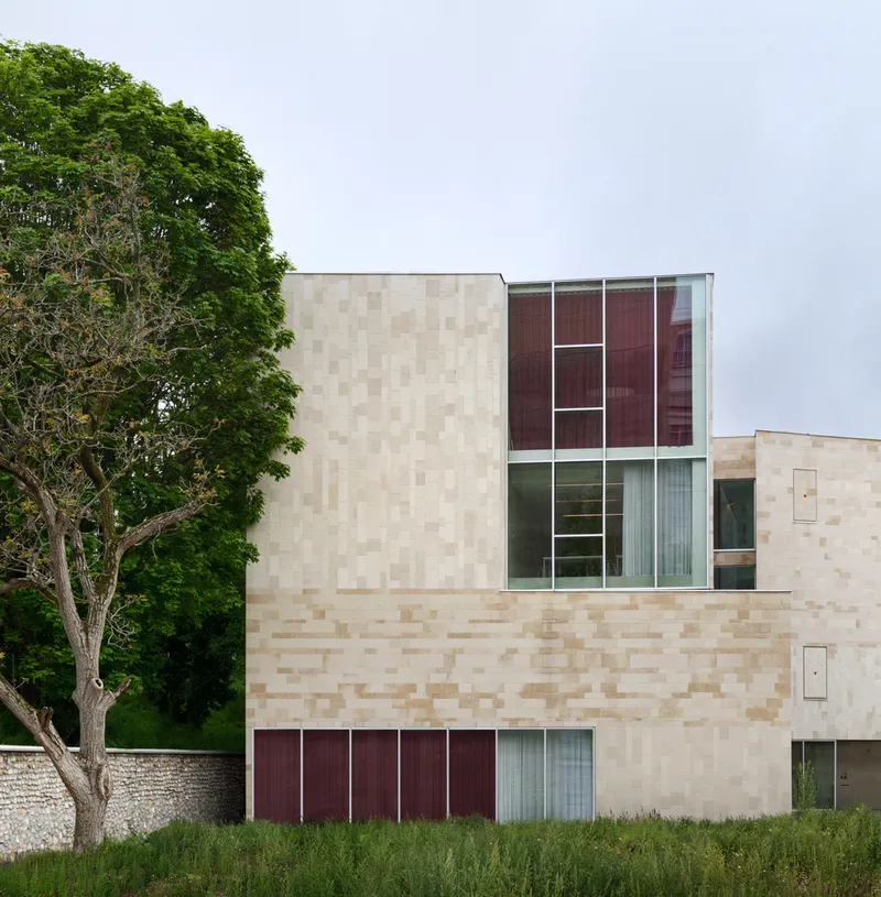 Exterior facade with checkerboard sandstone blocks and burgundy glazed panels beside a mature green tree