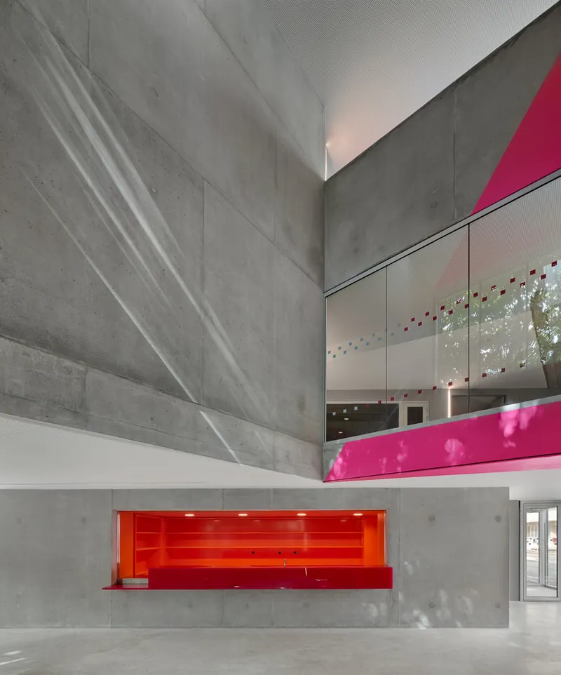 Double-height atrium with exposed concrete walls and a red-lit recessed niche below a magenta balcony