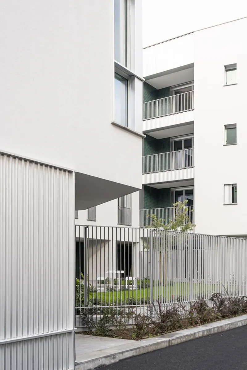 Courtyard view with stacked balconies, vertical metal railings and planted beds along the ground level
